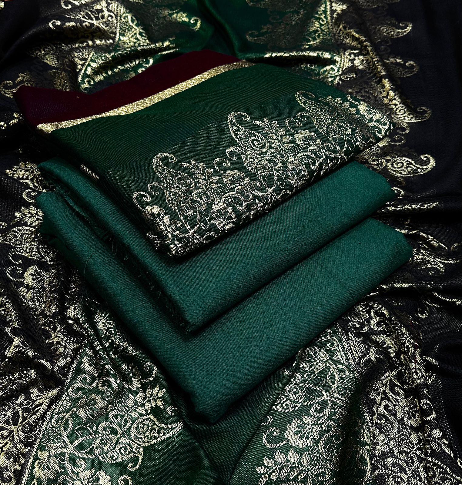 Green fabric with intricate white patterns on a dark, patterned background