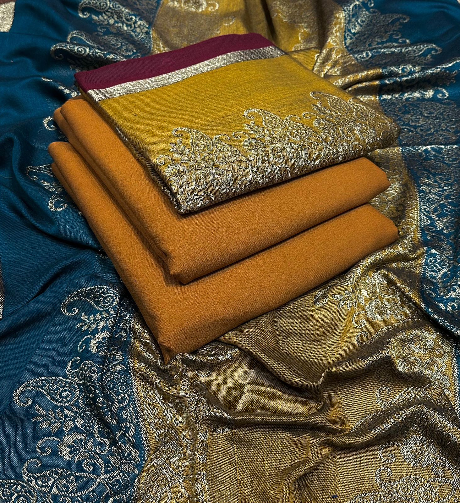 Stack of folded fabric with intricate patterns on a blue and gold background