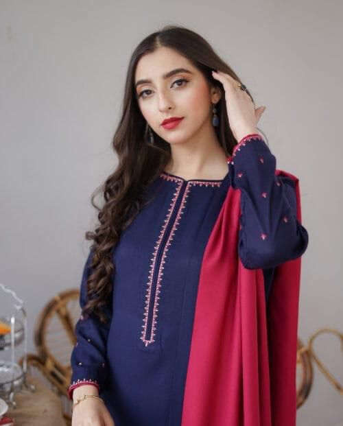 Woman wearing a blue embroidered top with a red scarf against a neutral background.Elegant Pakistani winter 3pc suit in linen fabric