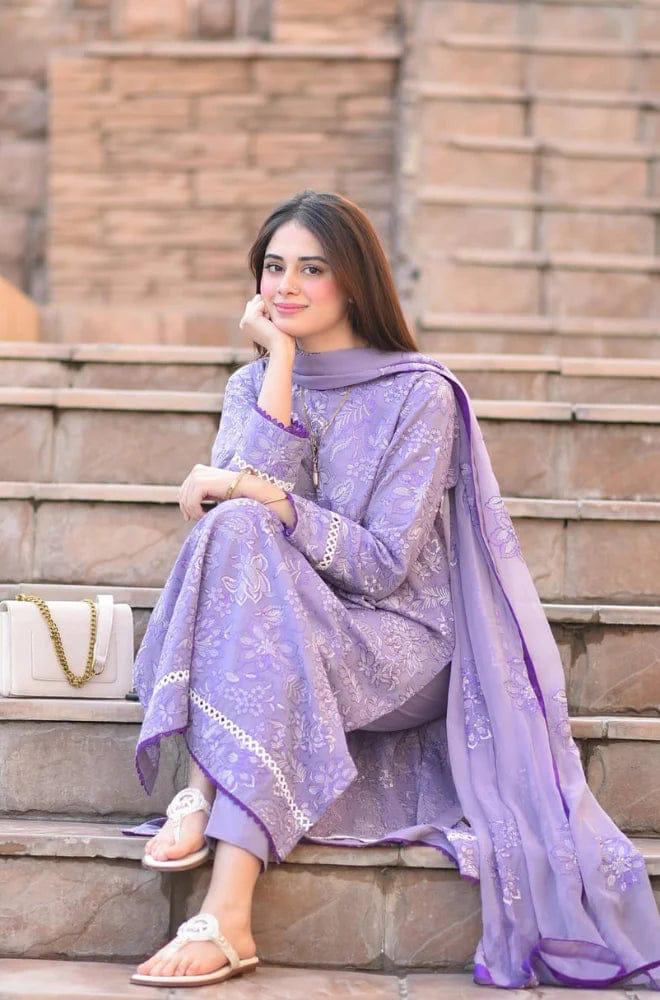 Woman in a purple traditional outfit sitting on steps with a stone wall background.
Elegant Pakistani winter 3pc suit in linen fabric