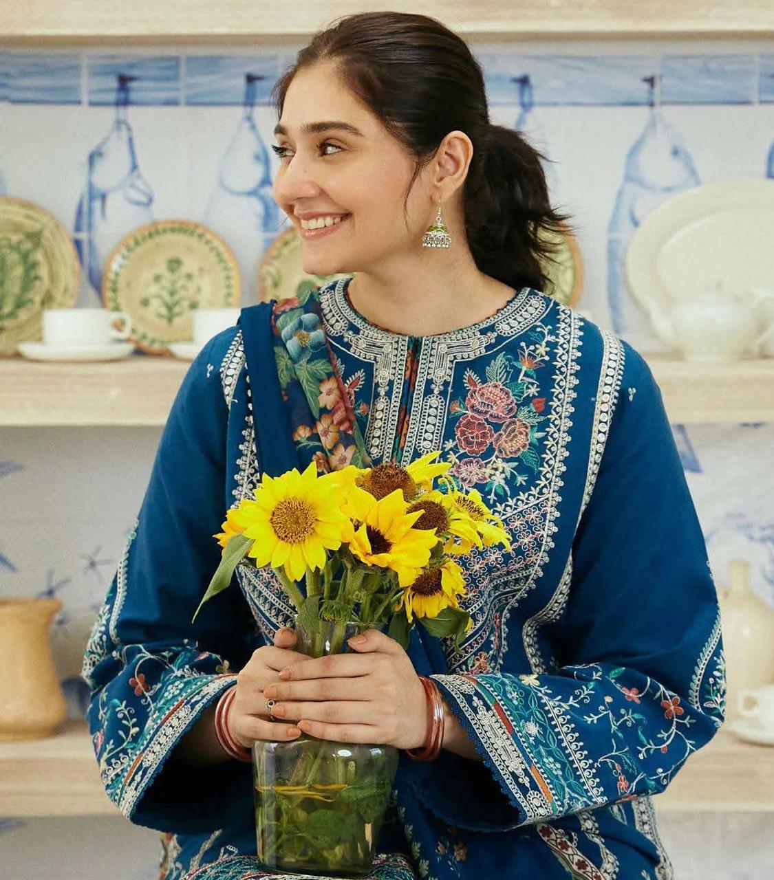 Woman in traditional embroidered outfit holding a vase of sunflowers in a kitchen setting.
Elegant Pakistani winter 3pc suit in linen fabric