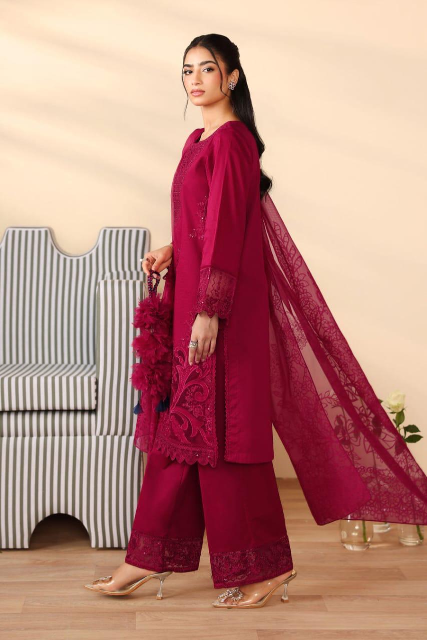 Elegant Pakistani winter 3pc suit in linen fabric.Woman in a magenta traditional outfit with a sheer dupatta, standing against a beige wall.